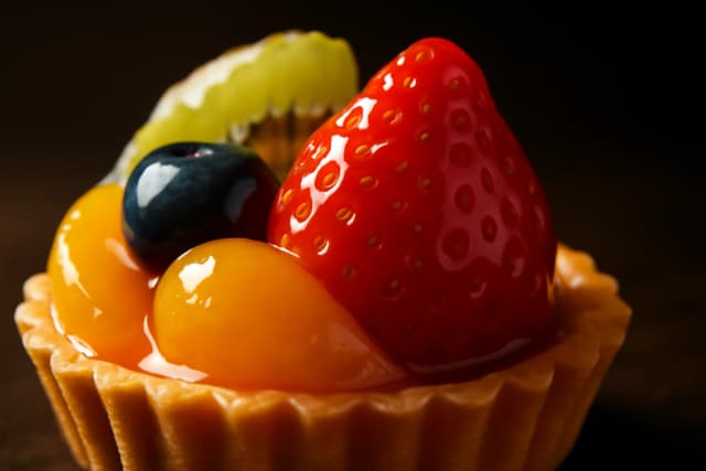 A beautifully plated gourmet dessert, a colorful fruit tart with glossy glaze, captured in a macro shot with a shallow depth of field, bright, warm studio lighting, dark background, luxury food photography